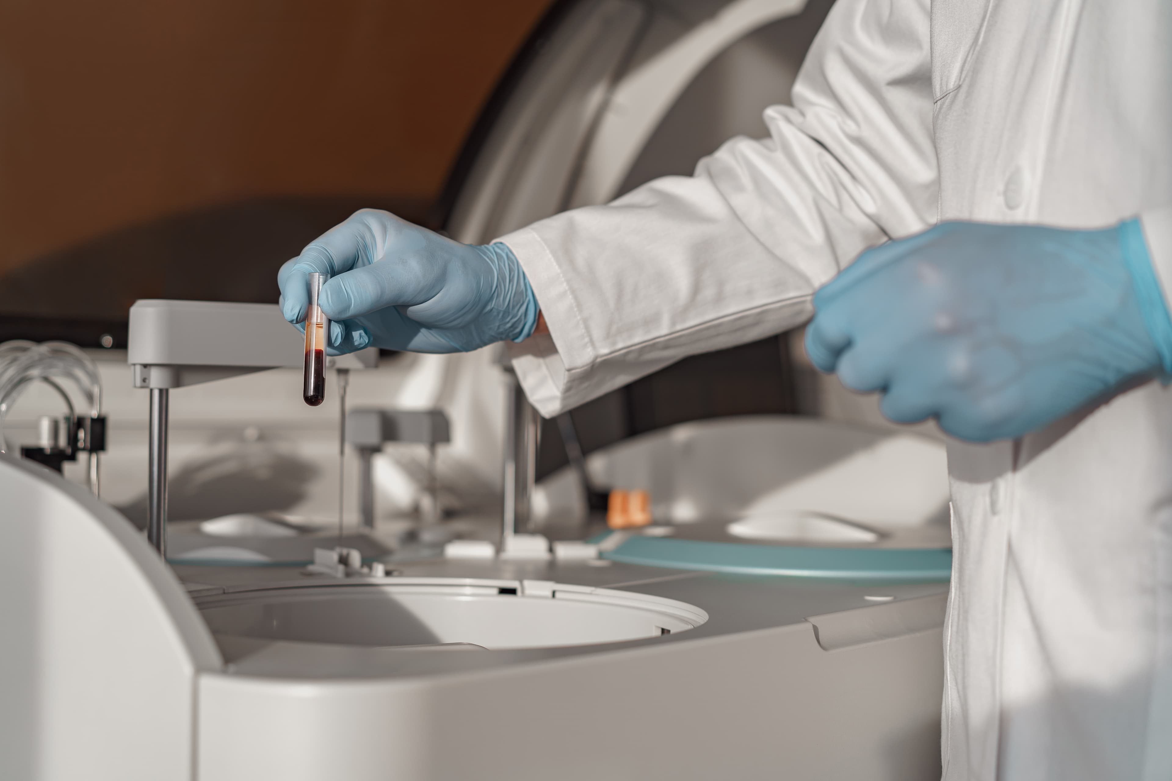 Dłonie w rękawiczkach przy próbce i aparaturze laboratoryjnej