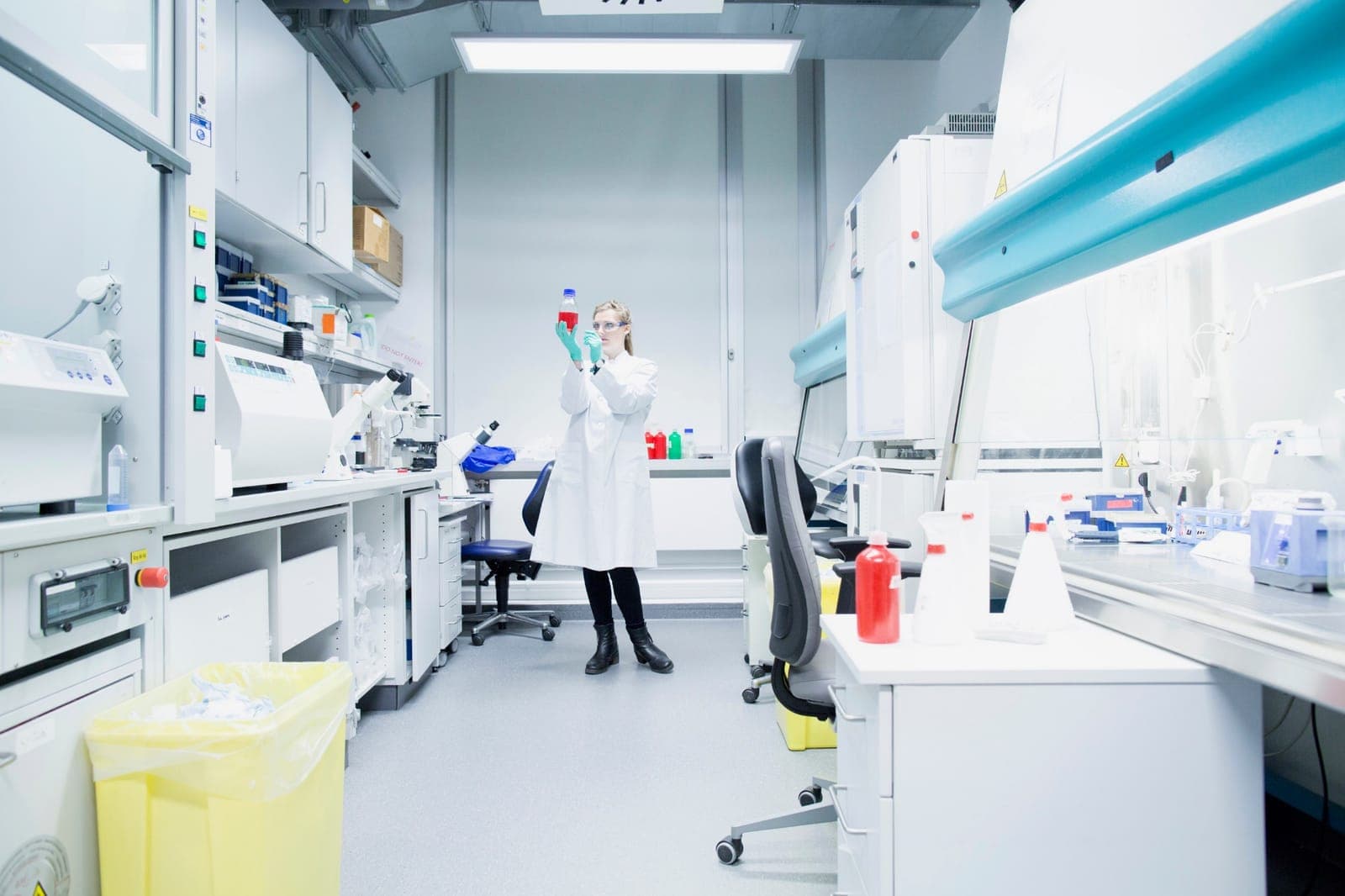 Laborantka ocenia butelkę z roztworem w pracowni z komorami i aparaturą laboratoryjną