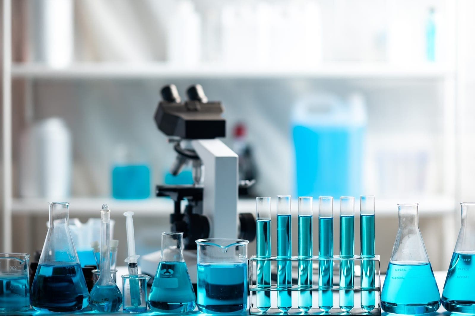 Szkło laboratoryjne z niebieskim roztworem i mikroskop na stole laboratoryjnym