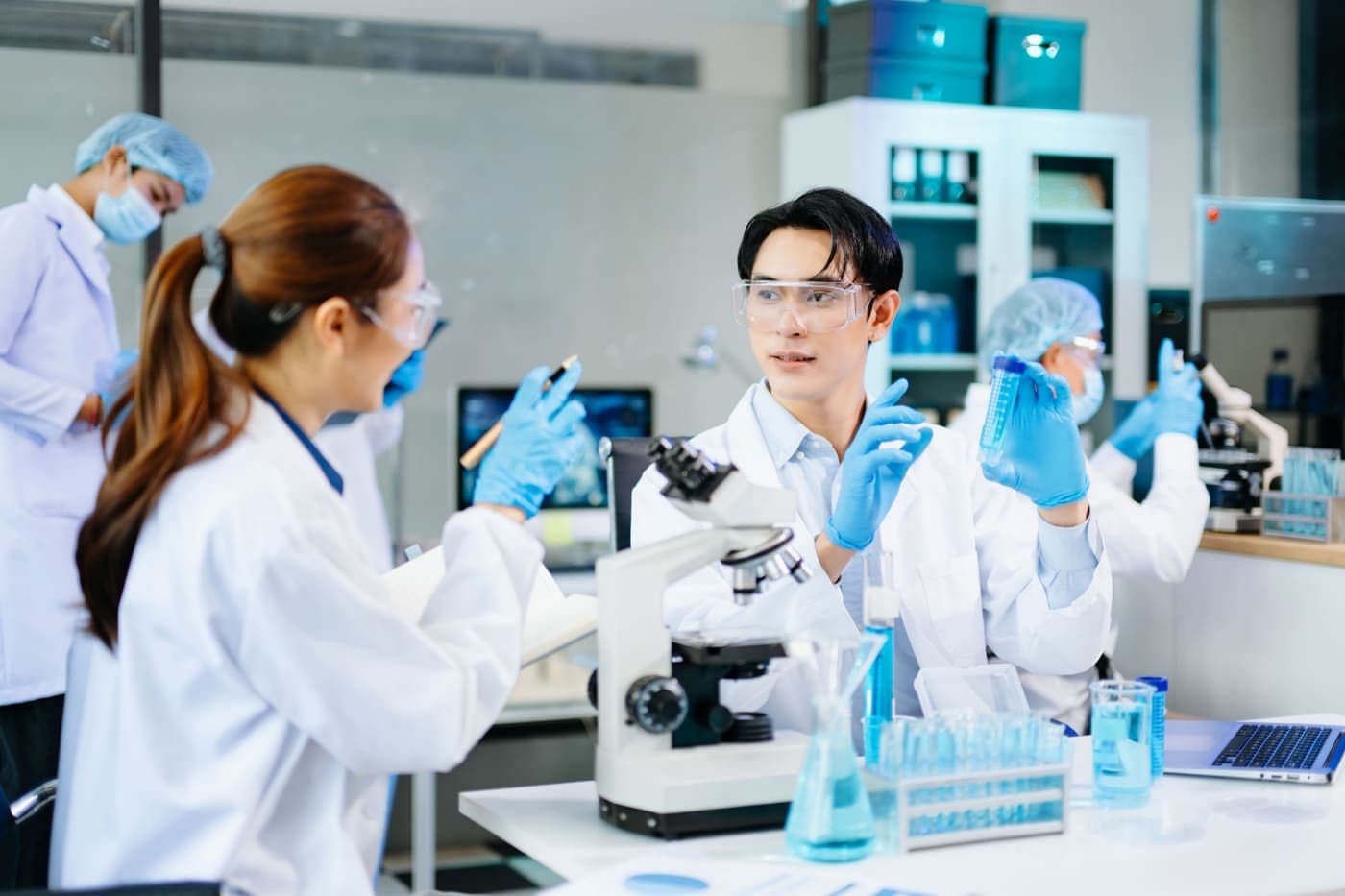 Zespół laboratoryjny w okularach ochronnych rozmawia przy mikroskopie i probówkach