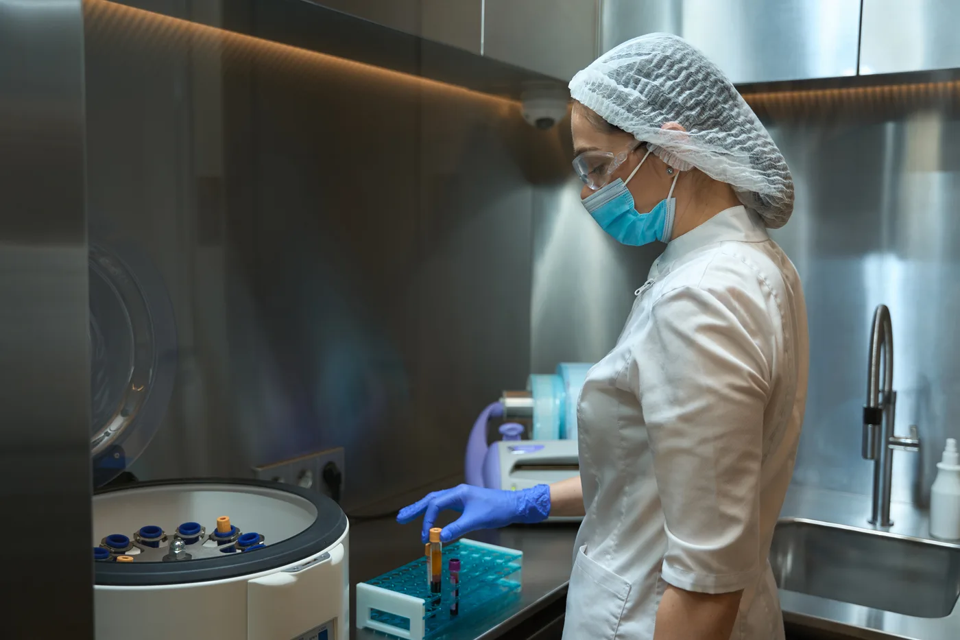 Pracownica laboratorium w odzieży ochronnej przy próbkach i wirówce